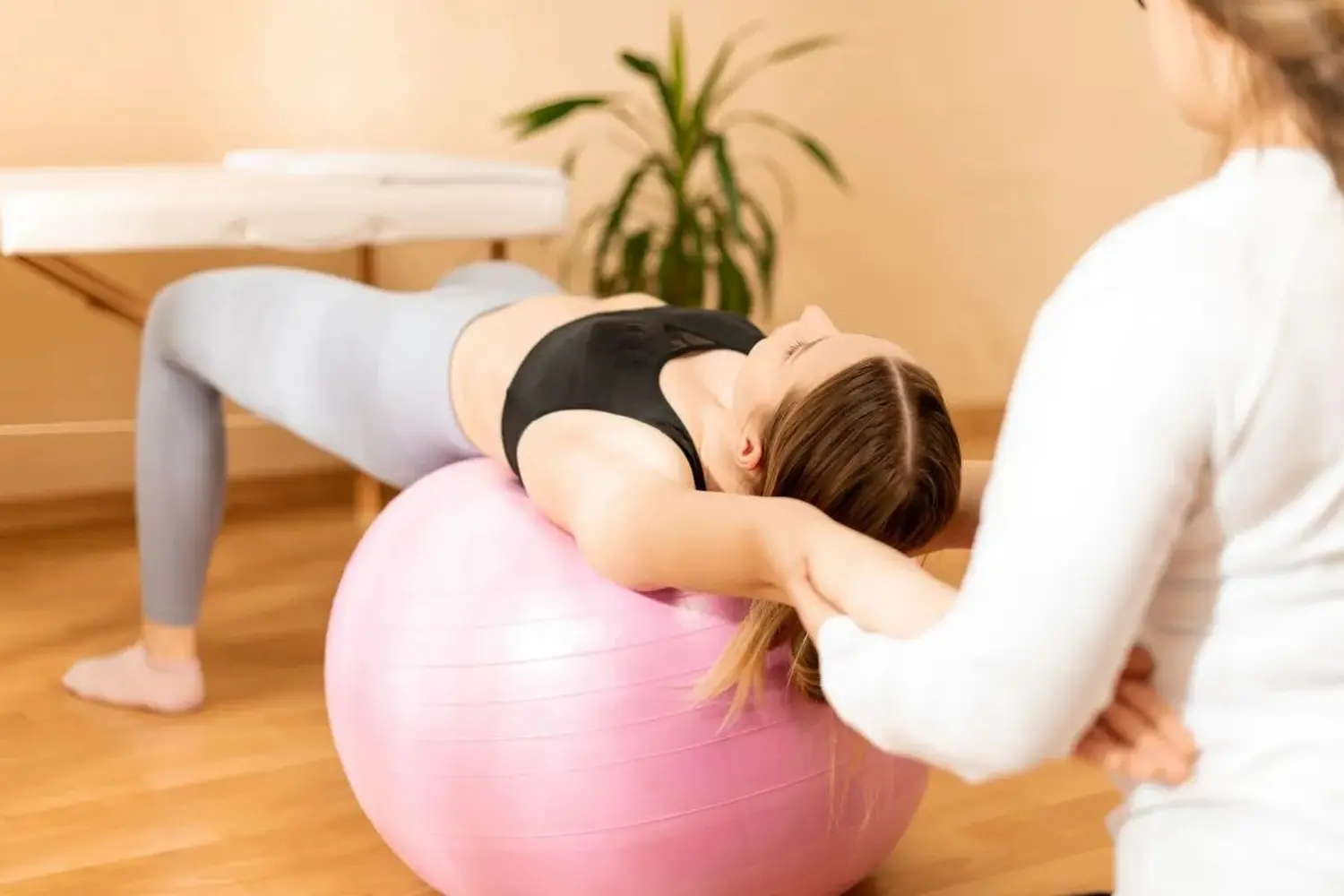 Physiotherapist working with young female client on core strength using fitball. Rehabilitation and physiotherapy background. 